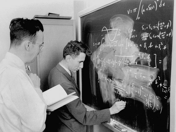 The black-and-white photograph shows two men in suits intently working through complex mathematical equations on a chalkboard, with one writing formulas that include integrals and trigonometric functions. The scene captures Claude Shannon in an academic setting, illustrating the foundational work in information theory that earned him the title "father of the digital age."