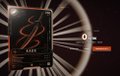 A dark product shot featuring an ornate red and gold 'B' monogram emblem, likely a luxury brand logo, set against a black background with radiating light effects.