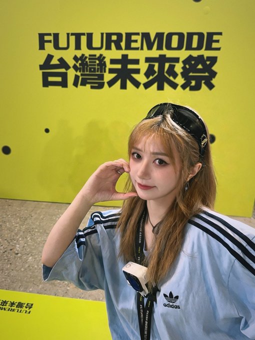 A woman in a light blue Adidas shirt poses in front of a bright green sign reading “FUTUREMODE 台灣未來祭” (Taiwan Future Festival).