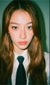 A young girl with long, wavy brown hair wearing a white shirt and dark tie poses for a portrait against a green background, presenting a matured appearance that aligns with the post's playful question about "Luna all grown up."