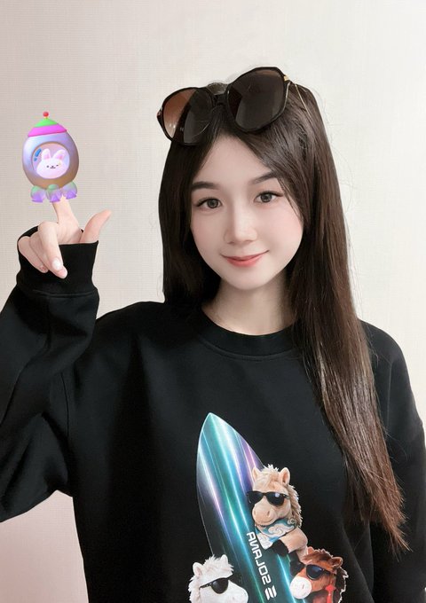 A young woman with long dark hair, sunglasses perched on her head, poses with a peace sign while wearing a black sweatshirt featuring alpaca characters and the text "AVENUE JOE 23." She holds up a small SOL (Solana mascot) figurine, matching her caption thanking Solana for the hoodie gift.