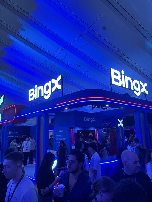 A crowded event space is illuminated in blue lighting with illuminated 'BingX' signs displayed prominently above a trading platform booth.