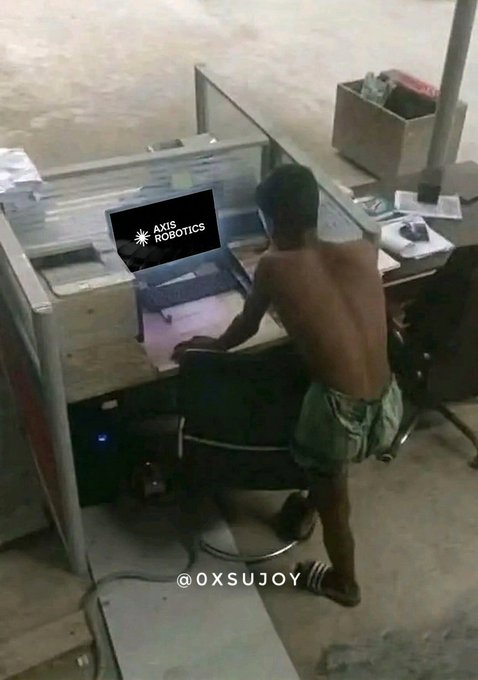 A shirtless person in shorts sits on a chair at a desk with a computer displaying an "AXIS ROBOTICS" logo, with the handle @OXSUJOY at the bottom.