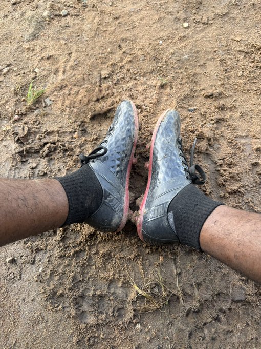 A pair of muddy black Nike football boots (with "FLY" text visible) worn with black socks rests on a dirt field, showing the aftermath of a tough pickup game. The post humorously blames "web3" for the poster's exhaustion and dizziness after barely lasting 10 minutes on the field for the first time in over a year.