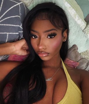 Trinity Tatum takes a close-up selfie while lounging on a bed, wearing a yellow top and a delicate name necklace. The image complements the post highlighting her leading 89% odds on Polymarket to win Love Island USA Season 8 before Sunday's finale.