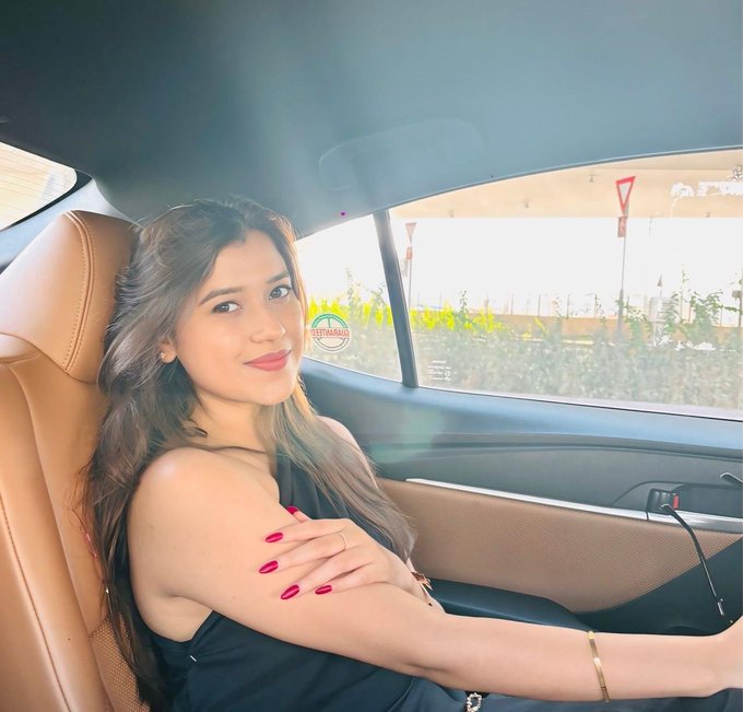 A young woman with long brown hair, red lipstick, and matching red nails poses in the driver's seat of a luxury car, smiling at the camera. The image complements the post's milestone of "5 years in crypto," visually representing one of the achievements mentioned—her first car.