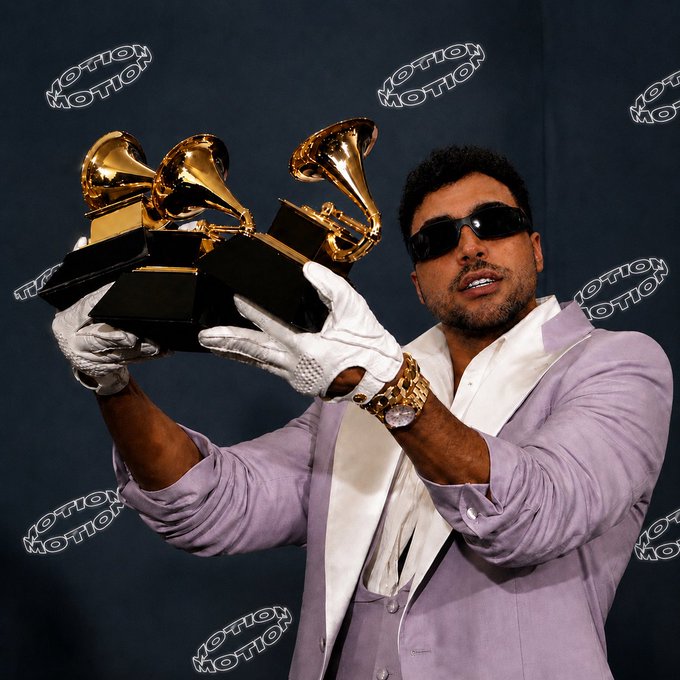 The image shows a man wearing sunglasses and a lavender suit with white gloves, proudly holding two Grammy trophies, while the post referencing "$MOTION" suggests a connection to the artist or brand "Motion," whose name is repeatedly watermarked across the photo in a stylized font.