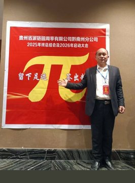 A man in a dark suit stands pointing at a red banner displaying the pi (π) symbol with Chinese text for a 2025 summary and 2026 kickoff meeting.