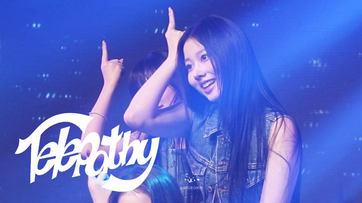 Concert photo of a smiling young woman with long dark hair in a denim vest making a finger-gun gesture, with 'Tabothy' stylized text overlaid on the left.