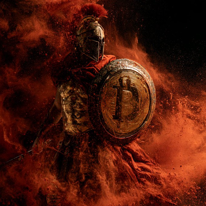 A Spartan warrior stands defiant amid a swirling cloud of orange dust, holding a battle-scarred shield emblazoned with the "B" Bitcoin symbol, embodying unwavering resilience and conviction. The image mirrors the post's message of enduring commitment—"Still here. Still stacking. Still learning. Still focused. Still know what I hold."—by portraying a steadfast guardian who knows exactly what he defends.