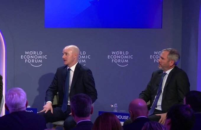 Two men in suits sit on a panel at the World Economic Forum, with the organization's logo visible on the backdrop behind them. The image appears to relate to the announcement about Coinbase and Ripple attending a White House crypto meeting, as such forums often involve key financial and cryptocurrency industry figures.