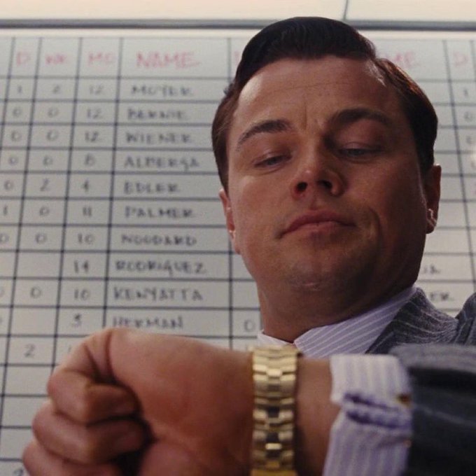 A cinematic shot of Leonardo DiCaprio's character checking his gold watch in front of a scoreboard, a famous scene from the movie 'The Wolf of Wall Street.'