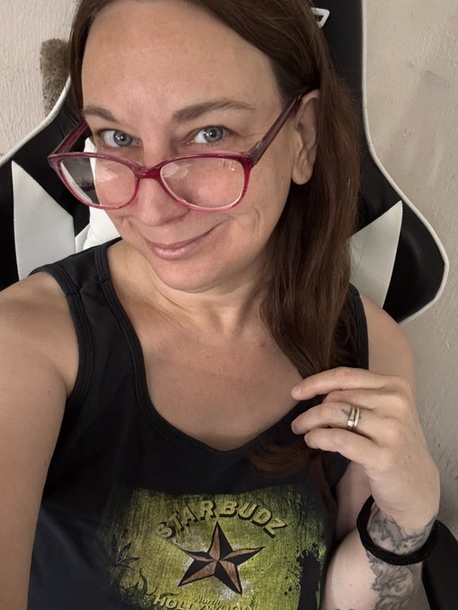A woman with red-framed glasses and a black "Starbuds Hollywood" tank top smiles at the camera, playfully hinting at a hidden crypto gem discovery with her post about finding the "next 100x."