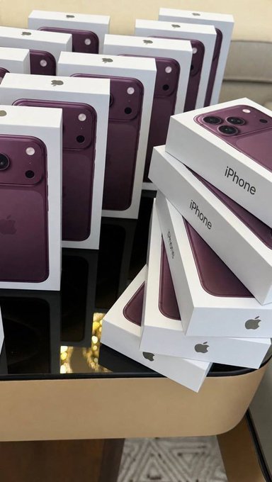 Multiple boxes of purple iPhones, likely the iPhone 14 Pro in Deep Purple, stacked on a reflective surface.