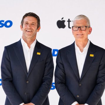 Two men in dark suits with yellow lapel pins stand smiling in front of a backdrop featuring the Apple logo and "SOSO" branding. The polished, corporate setting contrasts with the post's focus on market-moving economic news, including the upcoming August jobs report and Federal Reserve meeting.