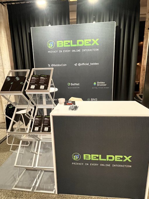 A booth display for 'BELDEX' with the tagline 'PRIVACY IN EVERY ONLINE INTERACTION', featuring a banner with handles @BeldexCoin and @official_beldex, promoting BelNet and Beldex Browser, alongside promotional flyers and a branded counter.