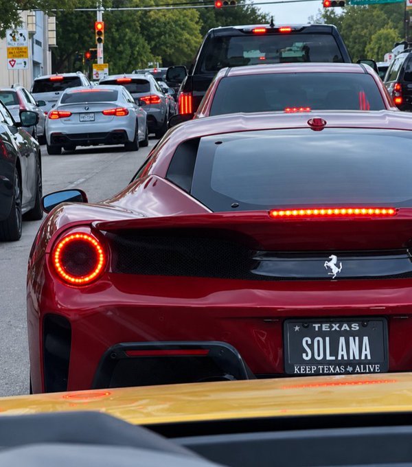 A red Ferrari is stopped in traffic behind other cars. The Texas license plate says 'SOLANA' with the frame 'KEEP TEXAS ALIVE.'