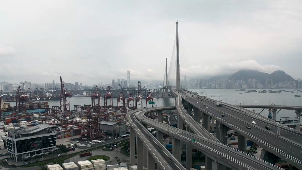 The image shows a cityscape with a large highway overpass, featuring multiple lanes for traffic flow. The scene also includes several cranes and buildings, indicating an industrial area. The caption provided seems unrelated to the image or its content.