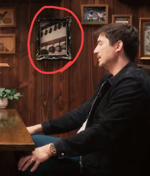 A man in a dark jacket sits at a wooden table, with a framed picture of fruit (apples and pears) hanging on the wood-paneled wall behind him, circled in red. The "Early not wrong btw" caption suggests the fruit imagery symbolizes being "ahead of the game" or early to a prediction/trend.