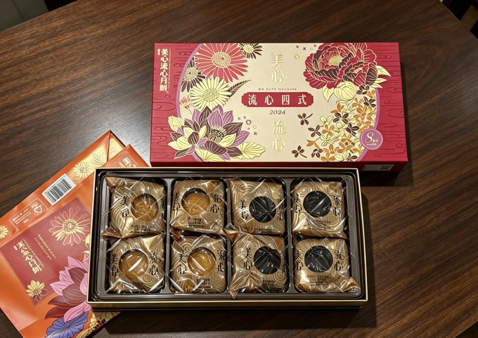 A box of Maxim's (美心) "Mei Xin Liu Xin" (流心四式) mooncakes is displayed, featuring 2024 designs with assorted flavors (4 pieces visible) and 8-piece packaging shown alongside a red floral promotional booklet. This connects to the post as the recipient was pleasantly surprised to receive this Hong Kong Maxim's mooncake airdrop after investing in $IGNIX.