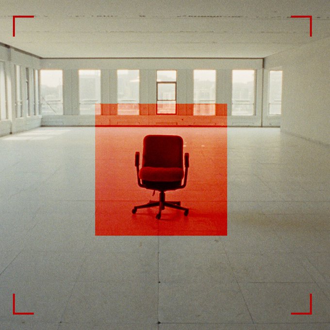 An empty, sunlit office room with a red office chair highlighted inside a red detection box, framed by red camera viewfinder corner brackets in a vintage film aesthetic.