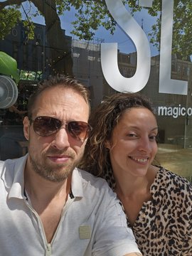 A man and woman smile in front of an Adidas store in Amsterdam, with "$UL" and "magic" text visible in the window.