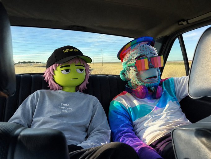Two characters wearing Robinhood-inspired hats and apparel—one with a "HOOD UP" cap and "TRG1B Robinhood 2024" sweatshirt, the other in a furry hat with rainbow shutter shades and headphones—sit in the backseat of a car, visually promoting the "Robinhood NFTs" giveaway mentioned in the post.