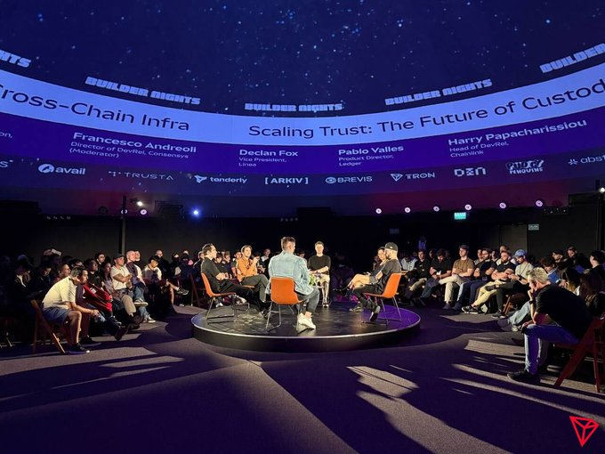 A panel discussion titled "Scaling Trust: The Future of Custody" takes place at a "Builder Nights" event, featuring speakers Francesco Andreoli (Director at Delphi, Consensus Moderator), Declan Fox (COO, Persona), Pablo Valles (Product Director, Ledger), and Harry Papacharissiou (Head of DeFi, Chainlabs). The image shows panelists seated on a stage surrounded by an audience, suggesting a discussion about decentralized finance and digital asset custody infrastructure—aligning with the post's theme of cryptocurrency serving as essential financial infrastructure in emerging markets.