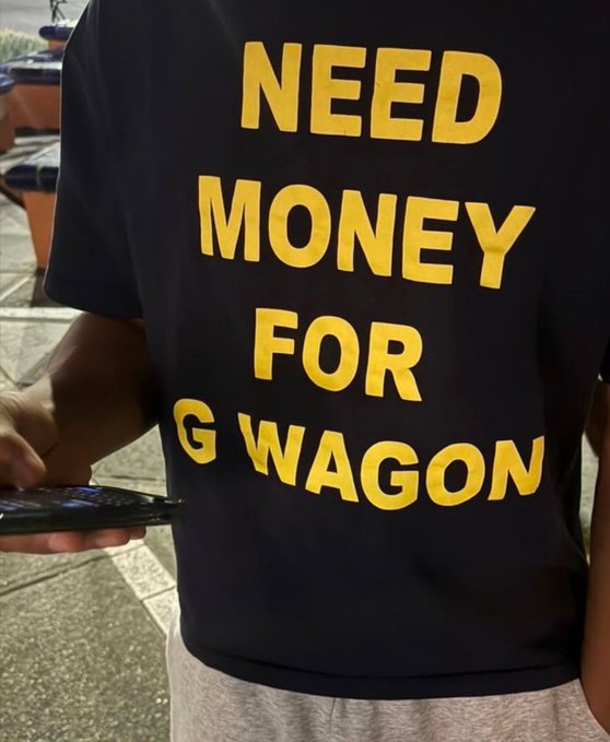 A person wearing a black t-shirt with bold yellow text reading "NEED MONEY FOR G WAGON" holds a smartphone, visually echoing the "ASAP" urgency expressed in the post.
