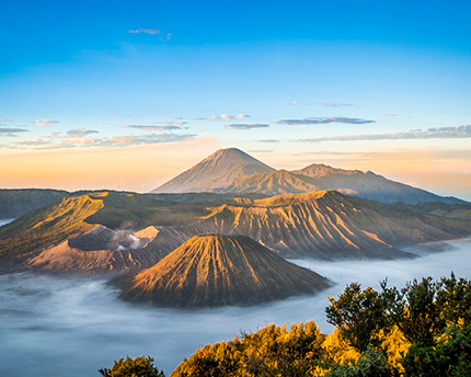 A stunning landscape view of a volcanic mountain range at sunrise, with mist rolling through the valleys beneath a clear blue sky.