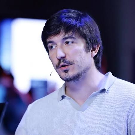 A man with dark hair, a goatee, and a light-colored sweater looks off to the side, appearing thoughtful or mid-conversation. The image likely depicts Vlad Tenev, the Robinhood CEO referenced in the accompanying post about the company's blockchain and its potential for memes.