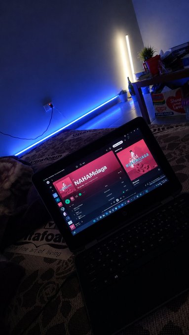 A photo of a tablet displaying a music streaming app called "NAHAMsiaga" on a bed with blue ambient LED lighting in the background.
