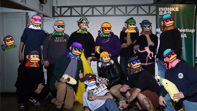 A group photo of people at a meetup, with their faces covered by CryptoPunk-style NFT avatars; a banner in the background reads 'MONKE 2024 Meetup' and 'TRADERS' appears on screen.
