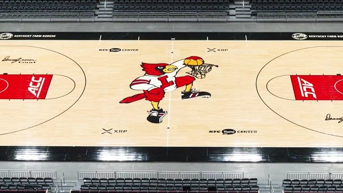The image shows the KFC Yum! Center basketball court featuring a large red cardinal mascot at center court, with XRP branding prominently displayed in multiple spots and "KFC Yum CENTER" text along with "Kentucky Farm Bureau" signage on the sidelines. This visual directly illustrates the post's claim of Ripple's XRP logo being incorporated into the Louisville basketball court design.