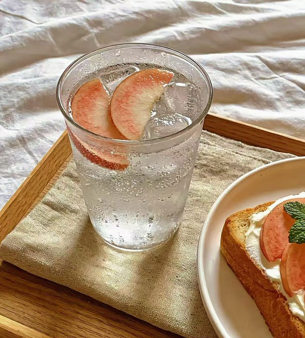 A glass of sparkling water with peach slices sits on a wooden tray next to a plate of toast topped with cream and peach slices, evoking a fresh and deceptively innocent presentation. The image visually contrasts the polished, fruit-laden surface with the post's underlying message: TermMax Alpha's dual-currency product appears harmless and even appetizing, but—like the clear drink hiding its structure—it's essentially a repackaged option-selling strategy that profits in both directions.