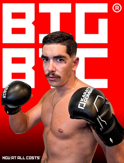 A boxer with a mustache and black Karane Combat gloves poses in front of a red 'BIG BIG' branded background, with the slogan 'NOW AT ALL COSTS' at the bottom.
