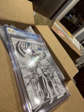 A CGC 9.9 graded comic book of G.I. Joe is shown resting in a cardboard box, encased in a protective plastic slab.