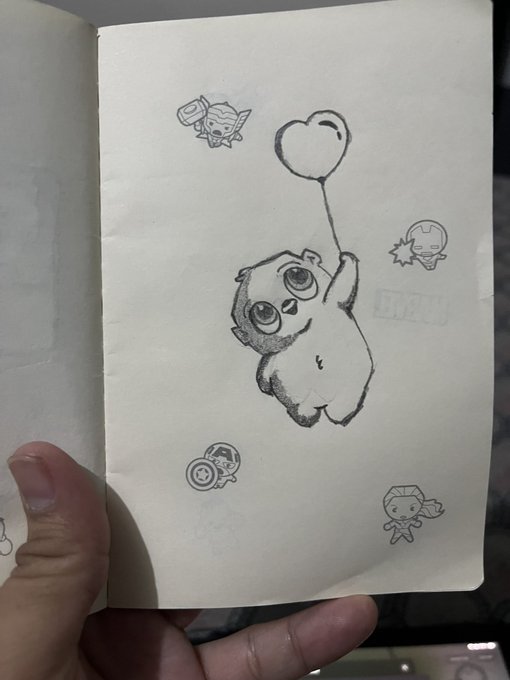 A pencil sketch in a notebook of a cute cartoon character holding balloons, surrounded by smaller doodles of similar characters.