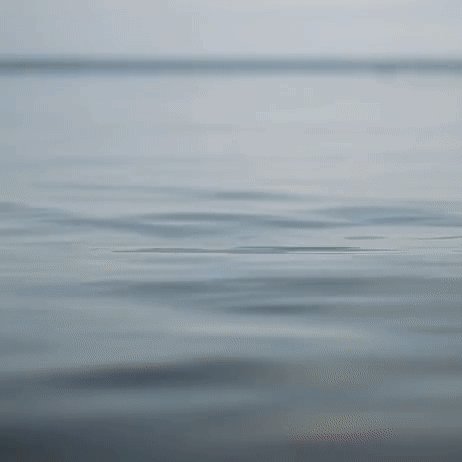 The image shows a serene ocean scene with calm water, where ripples are visible on the surface of the water. The background features a sky that appears hazy or blurred, adding depth to the overall composition. The photo has been edited to emphasize the tranquility and peacefulness of the ocean, creating an atmosphere of relaxation and contemplation.