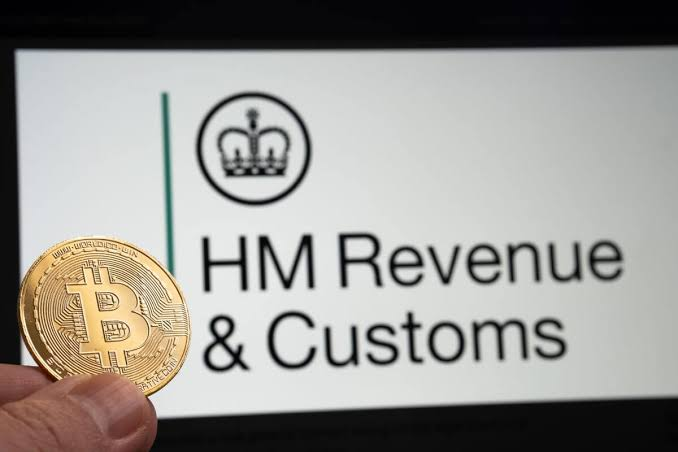 A gold Bitcoin coin is held in front of a screen displaying the "HM Revenue & Customs" logo, symbolizing the UK's tax authority's increased scrutiny of cryptocurrency transactions. The image visually reinforces HMRC's crackdown on crypto investors, as over 502 individuals have voluntarily paid £8 million in back taxes amid the agency's heightened monitoring efforts.