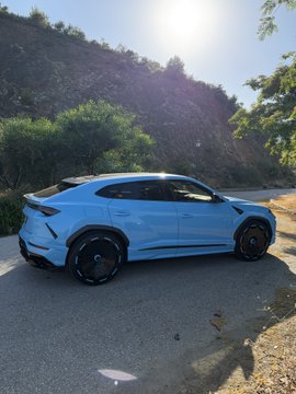A white Lamborghini Urus is parked on a sunlit mountain road, casting a sharp shadow. The image contrasts the sleek, high-performance luxury of the car with the post's message about the often-overlooked mental health struggles behind the crypto lifestyle—highlighting that financial success doesn't shield you from emotional strain.