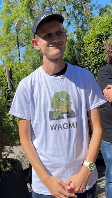 A young man wearing a black Nike cap and a white t-shirt featuring a graphic of Pepe the Frog giving a thumbs-up above the text 'WAGMI'.