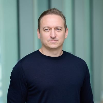 A man in a dark navy sweater stands against a teal curtain backdrop with a serious expression, accompanying a post declaring "We will win" with the $ICP ticker. The image shows a professional portrait, likely of the person making the bullish statement about the Internet Computer cryptocurrency.