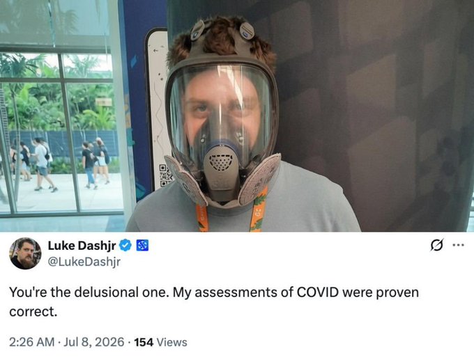 A tweet from verified user "Luke Dashjr" (@LukeDashjr), posted at 2:26 AM on July 8, 2026 with 154 views, features a photo of a man wearing a full-face respirator mask. The tweet reads: "You're the delusional one. My assessments of COVID were proven correct."