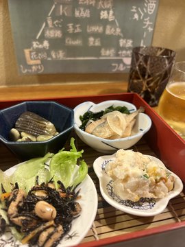 A traditional Japanese meal is served on a red tray featuring small dishes of hijiki seaweed, clams, greens, and tempura, with a chalkboard menu in the background listing drinks including "菊正宗" and "KIR BEER" at prices of 400, 500, and 200 yen. The setting reflects the post's narrative of a sake tasting experience at #STEPN酒場, where the user revisited a Japanese pub during a return trip from abroad to enjoy local food and drinks.