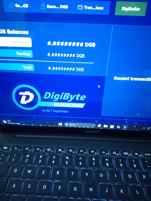 A photograph shows an AXIOO laptop displaying a cryptocurrency wallet interface for 'DigiByte BLOCKCHAIN v9.26.7 DigiDollar', with masked balance figures in DGB and sections for 'Send', 'Receive', 'Transactions', and 'Recent transactions'.