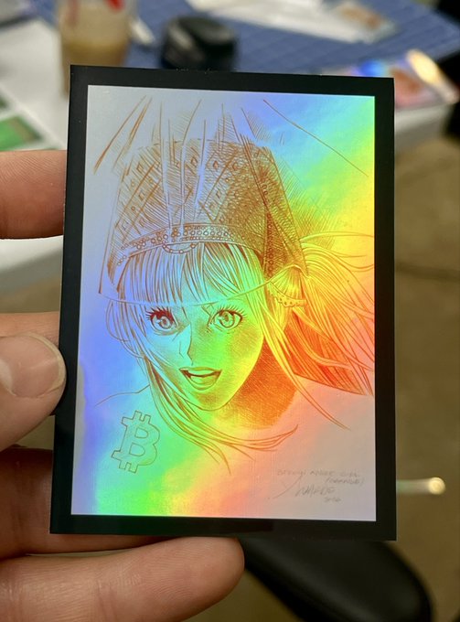 A hand holds a holographic sticker featuring an anime-style girl with a crown and a Bitcoin symbol, signed by the artist "VISHWA" dated 2023.