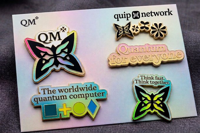 A collection of colorful enamel pins featuring butterfly logos and text like 'QM', 'quip network', 'Quantum for everyone', 'The worldwide quantum computer', and 'Think fast. Think together.' on an iridescent card.