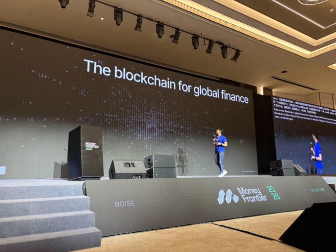 A speaker on stage at the Money 20/20 event presents "The blockchain for global finance," with the phrase displayed on a large screen behind him.