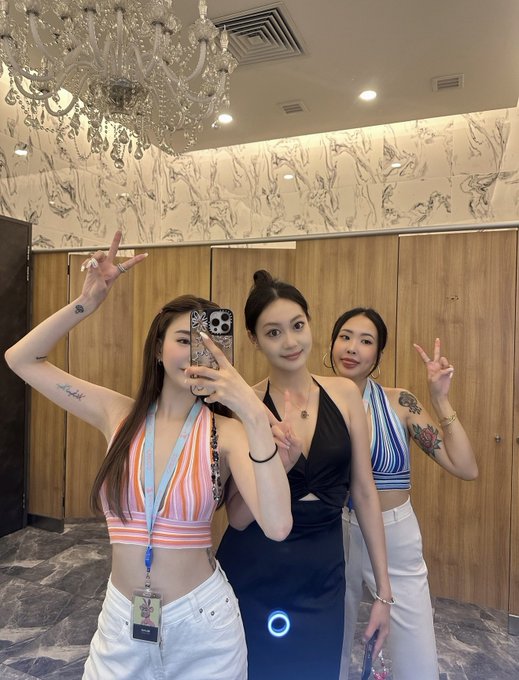 Three women pose for a mirror selfie in an upscale venue featuring marble walls and a crystal chandelier, with the text "TOKEN" partially seen on a wristband or badge. The caption reflects on attending NFT NYC in 2021 as their first major crypto/Web3 event, connecting the lively gathering shown to their nostalgic reminiscing about the early days of conference culture in the space.
